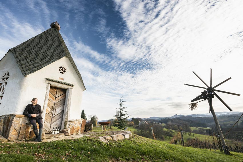 Winzer Reinhard Muster bei einer Kapelle mit Sicht auf die Weinberge der Steiermark und Klapotetz