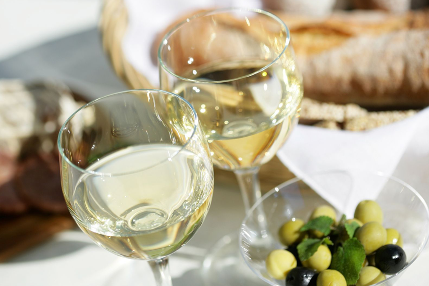 zwei Gläser mit Chardonnay, dahinter etwas Brot und vorne eine Schale Oliven