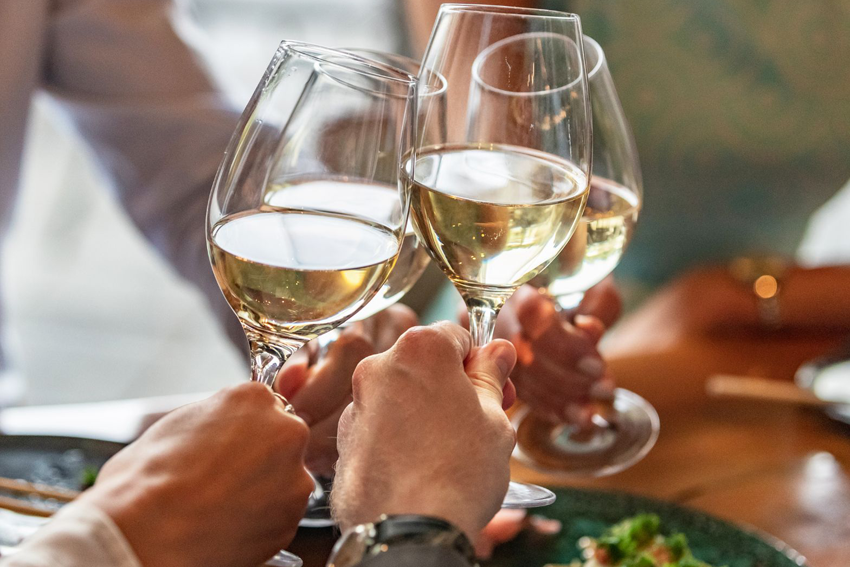 Vier Weingläser mit Weißwein stoßen an